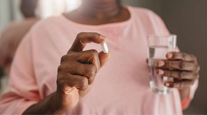 Older woman holding a white pill and a glass of water